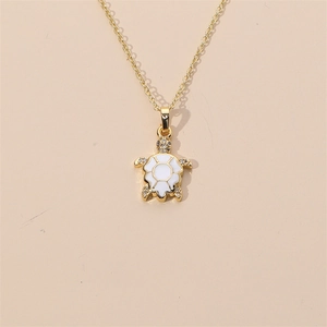 Gold plated turtle pendant necklace with white enamel and sparkling crystals on beige background
