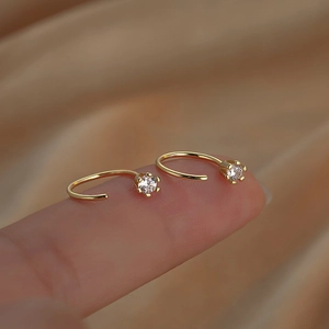 Minimalist gold C-shaped earrings with zircon accents shown held by a fingertip