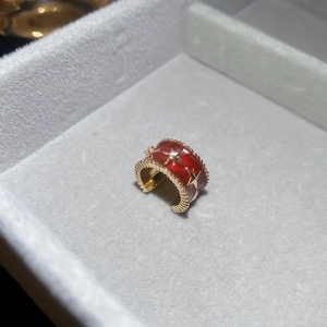 Macro view of red enamel star earring with gold bead edges in a grey jewelry box