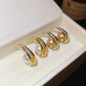 Macro shot of gold C-shaped pearl earrings with cubic zirconia in a jewelry box