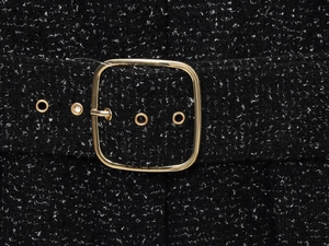 Détail de la ceinture en tweed avec boucle dorée et texture tissée sur tissu noir