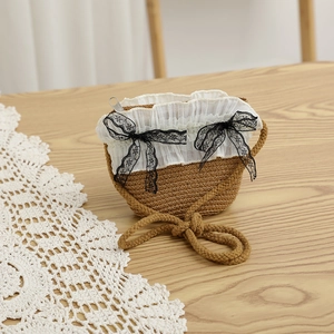 Vue détaillée d'un sac en paille pour enfants avec dentelle blanche et nœuds noirs sur bois