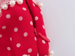 Dettaglio macro di tessuto rosso a pois bianchi con perle e cerniera posteriore