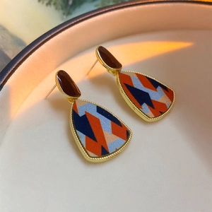 Detailed shot of gold-framed triangular earrings with orange, blue, and beige geometric inlay