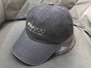 Detail of washed grey cotton baseball cap featuring colorful hearts and script embroidery