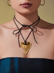 Detail of a gold fluid heart pendant on a black leather cord tied in a stylish bow