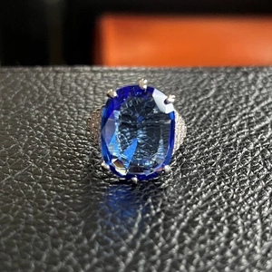 Macro di anello con topazio blu ovale, castone a sei griffe e pavé di piccoli diamanti