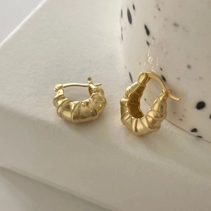 Close-up of golden croissant style earrings with textured spiral ridges on white surface