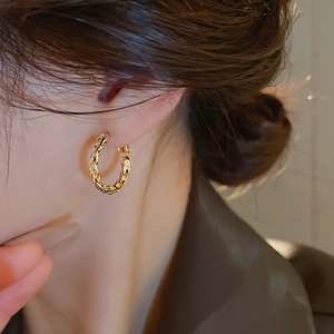 Close-up of elegant golden twisted rope hoop earrings worn by a model for a chic look