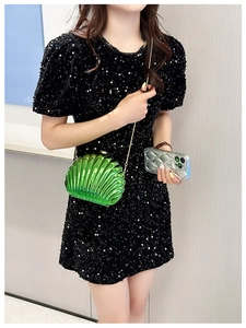 Detail of green shell-shaped acrylic clutch bag with a gold chain strap on a black dress