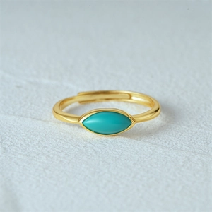 Close-up of golden adjustable ring with marquise turquoise stone on textured surface