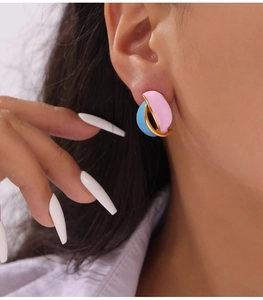 Close-up of pink and light blue enamel earrings with gold edges on a model's ear