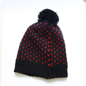 Nahaufnahme der schwarzen Strickmütze mit roten Herzen und flauschigem Bommel