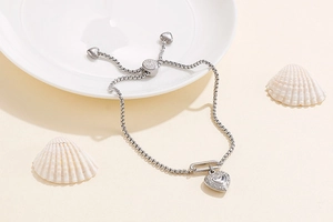 Detailed view of silver heart pendant bracelet with adjustable pull-chain on ceramic