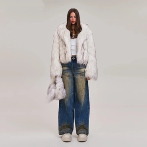 Woman in white faux fur coat and blue distressed wide-leg jeans against grey background