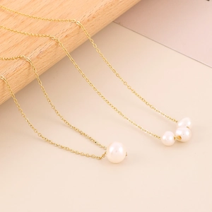 Detail of minimalist 18K gold plated titanium necklaces with shell pearls on wood