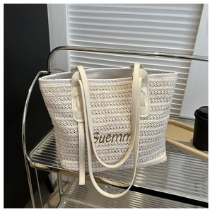 Detail of cream woven straw tote bag with brown leather handles and Suemm embroidery