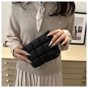 Detail view of a black quilted puffer clutch bag with a minimalist checkered pattern