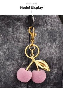 Close-up of pink flocked cherry charm with gold hardware on a textured handbag
