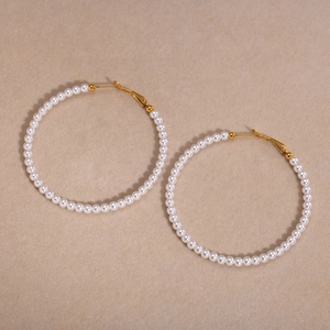 Detail of C-shaped hoop earrings featuring white faux pearls and gold-plated metal clasp