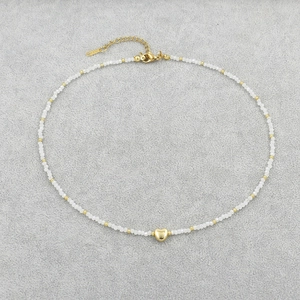 Detail of beaded necklace featuring white crystals and a polished gold heart pendant