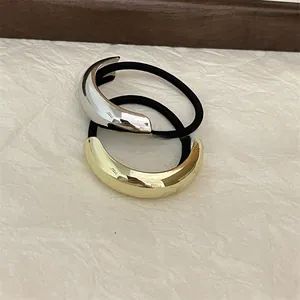 Polished gold and silver crescent metal hair ties with elastic bands on a beige base