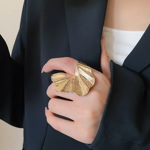 Close-up of golden fan-shaped flower ring with textured pleats on model's finger