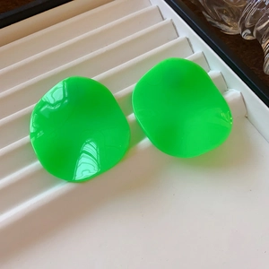 Detailed macro view of fluorescent green leaf-shaped resin earrings on white display tray