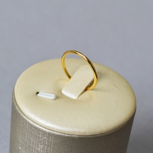 Macro shot of minimalist gold wave ring on beige display stand with metallic shine