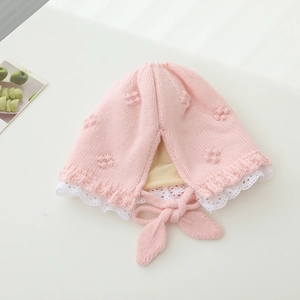 Detail of pink knitted baby bonnet with white lace trim and soft cotton lining