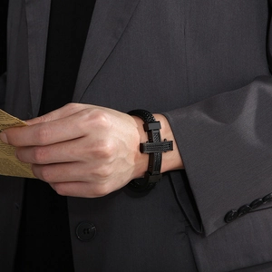Close-up of men's black braided leather bracelet with a steel cross on a model in a suit
