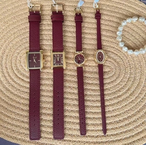 Group of burgundy leather straps watches with gold cases on a woven mat with pearl bracelet