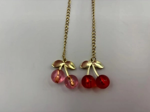Macro shot of red and pink cherry charms with gold metal leaves on a long chain