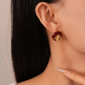 Close-up of a 3D gold bee on a deep red enamel round earring worn by a model