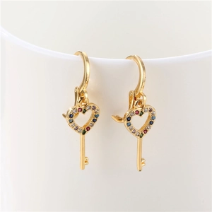 Golden heart key earrings with colorful cubic zirconia crystals on a white ceramic cup