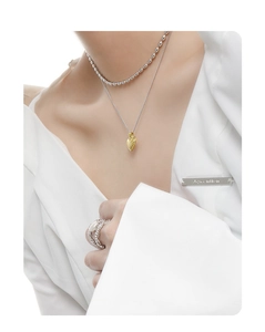 Detailed shot of gold heart pendant necklace styled with layered beaded silver chains