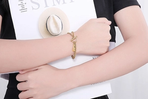 Detail eines goldenen zweilagigen Kettenarmbands mit Gitarren- und Taschenanhänger