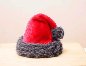 Detail of red plush Christmas hat with grey faux fur trim and pompom on wooden surface