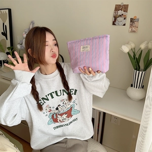 Close-up of pink and purple striped canvas makeup bag held by a model in a cozy setting