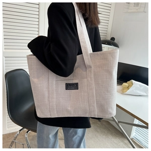 Detailed texture of a large light grey canvas tote bag worn by a model in a modern office