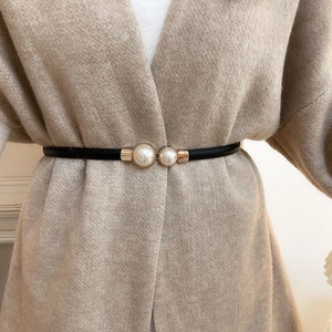 Detail of elegant black skinny belt with gold buckle and pearls on a beige cardigan
