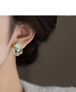Detail of flower-shaped pearl earring with green enamel and purple blossoms on model