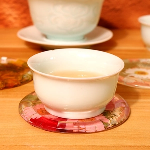 Detail of floral resin coaster with dried flowers and a ceramic teacup on wood