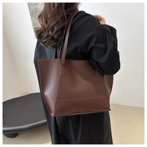 Detail of a large brown tote bag showing textured matte synthetic leather and fine stitching