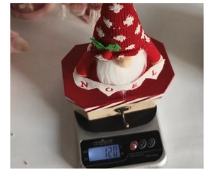 Detailed view of red Christmas gnome gift box on a scale showing 120g weight and Noel logo
