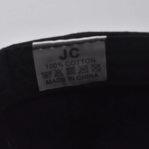Macro shot of 100% cotton wash care label and JC brand logo on black baseball cap
