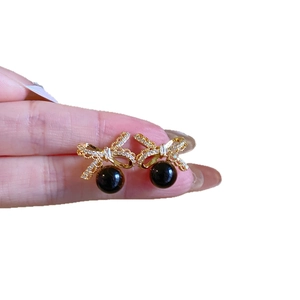 Elegant gold bow earrings featuring white crystals and a dark round pearl pendant