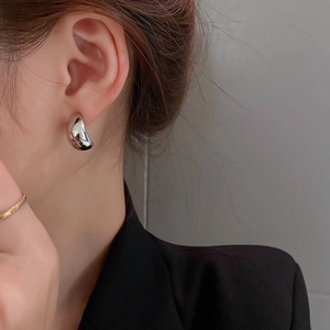 Close-up of minimalist layered silver metal hoop earrings worn by a model in soft light