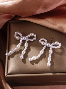 Macro detail of French bow earrings with white pearls and tassel on luxury silk background