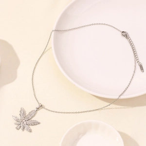 Macro detail of silver stainless steel necklace with maple leaf pendant on white plate
